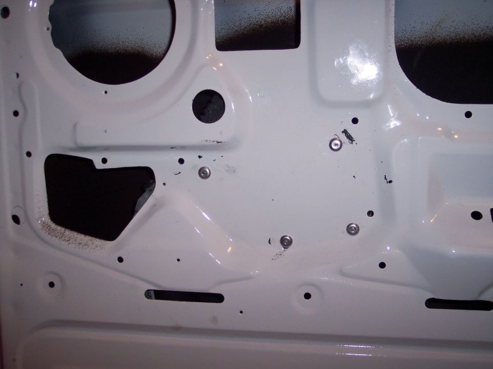 White vehicle door interior with black spray paint overspray and visible screw holes