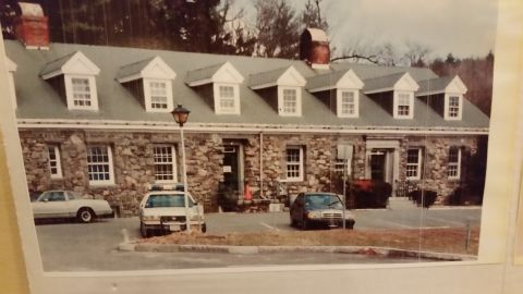 1991 Ford LTD Crown Victoria - A police car and two other vehicles are parked in front of a stone building with a long, sloping roof.