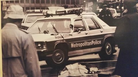 1991 Ford LTD Crown Victoria - Sepia photo of officers around a Metropolitan Police station wagon on a city street, not a technical document.
