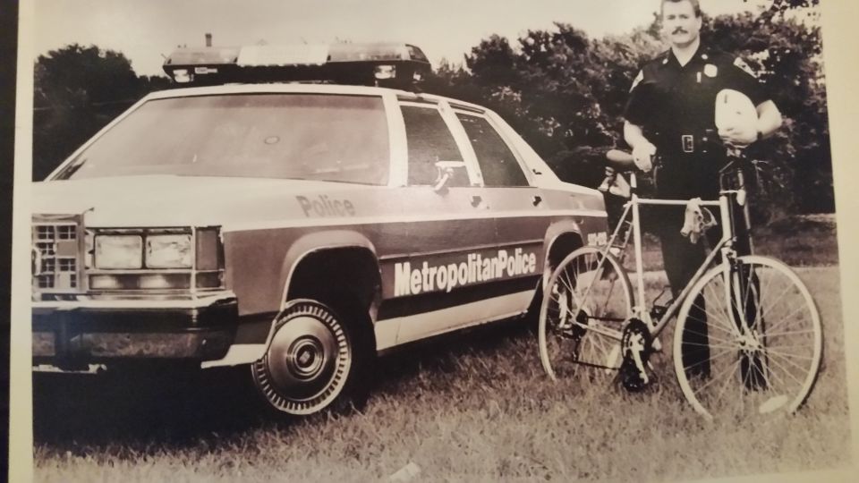 Vintage photo of a bicycle patrol officer next to a Metropolitan Police Crown Victoria
