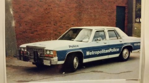1991 Ford LTD Crown Victoria - Photograph of a Metropolitan Police Ford LTD Crown Victoria patrol car parked against a brick building, not a technical document.
