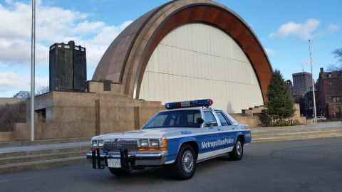 1991 Ford LTD Crown Victoria - Photograph of a Metropolitan Police Ford Crown Victoria patrol car near an outdoor amphitheater, not a technical document.