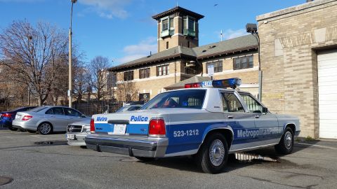 1991 Ford LTD Crown Victoria - Photograph of a Metropolitan Police Ford Crown Victoria patrol car parked near a brick tower, not a technical document.