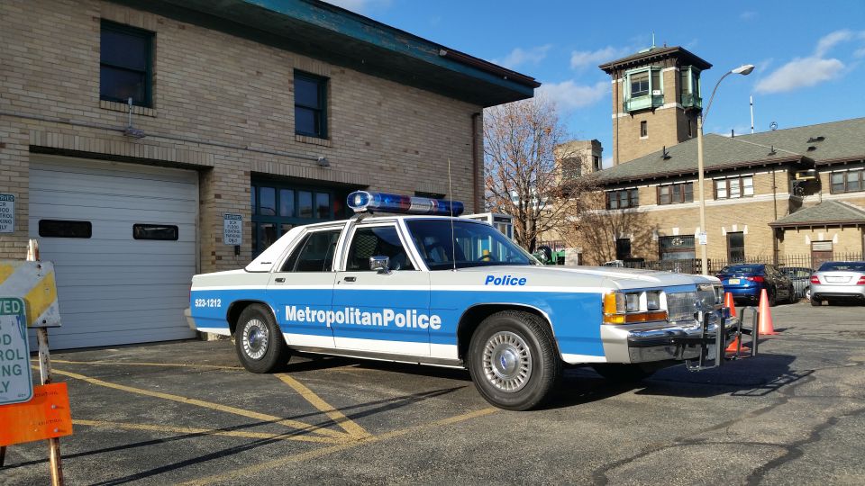 Blue and white 1955 sedan, side view, parked in front of a building with a garage door