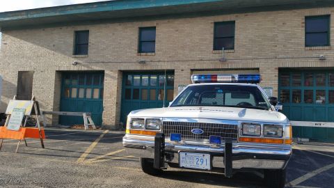 1991 Ford LTD Crown Victoria - A 1991 Ford Crown Victoria police car is parked outside a building with multiple garage bays.