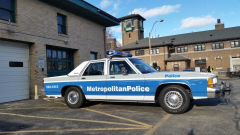 1991 Ford LTD Crown Victoria - A police car with 'Metropolitan Police' text and emergency lights is parked outside a brick building.