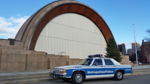 1991 Ford LTD Crown Victoria - A police car is parked in front of a building with a distinctive arched roof.
