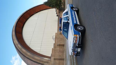 1991 Ford LTD Crown Victoria - A police car with 'Metropolitan Police' text on its side is parked near a building with a large, curved, copper-colored roof.