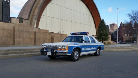 1991 Ford LTD Crown Victoria - A 1991 Ford Crown Victoria police car is seen parked in front of a large, modern building with a curved facade.