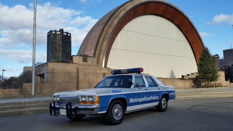 1991 Ford LTD Crown Victoria - A 1991 Ford Crown Victoria police car is parked in front of a modern building with a large arched facade.