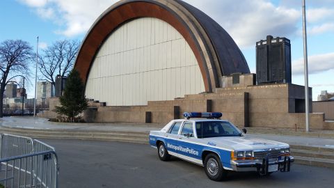 1991 Ford LTD Crown Victoria - A police car is parked in front of a large, modern building with a curved roof.