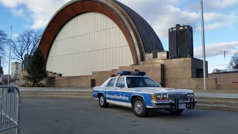 1991 Ford LTD Crown Victoria - A 1991 Ford Crown Victoria police car is parked in front of a large, modern building with a curved roof.