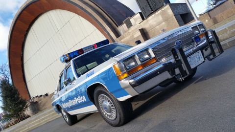 1991 Ford LTD Crown Victoria - A 1991 Ford Crown Victoria police car is parked in front of a large, curved building.
