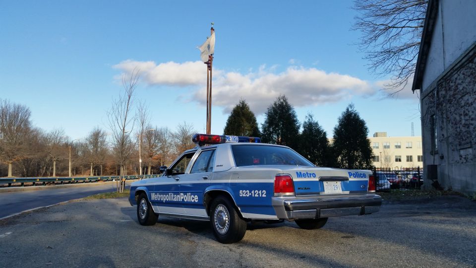 police car parked on asphalt, rear view. Has 'Metropolitan Police' and '523-1212' on the side