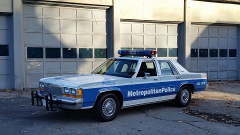 1991 Ford LTD Crown Victoria - This police car, identified as a 1991 Ford Crown Victoria, is parked outside a building with large garage doors.