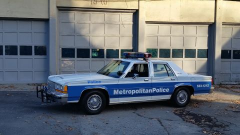 1991 Ford LTD Crown Victoria - This 1991 Ford Crown Victoria police car is parked in front of a building with large garage doors.