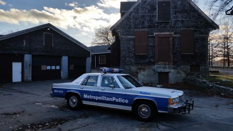 1991 Ford LTD Crown Victoria - A 1991 Ford Crown Victoria police car is parked in front of a weathered building with boarded-up windows.