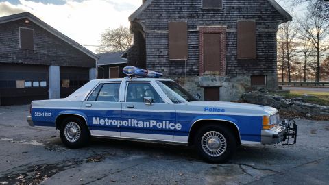 1991 Ford LTD Crown Victoria - This police car is parked in front of weathered buildings under a cloudy sky.