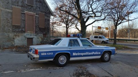 1991 Ford LTD Crown Victoria - Metropolitan Police Crown Victoria parked on a street next to an abandoned building, with a van visible in the distance.
