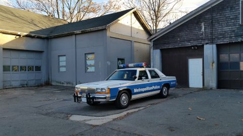 1991 Ford LTD Crown Victoria - A police car with a light bar is parked in front of a building with garage doors.