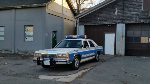 1991 Ford LTD Crown Victoria - A 1991 Ford Crown Victoria police car is parked in front of a building with garage doors.