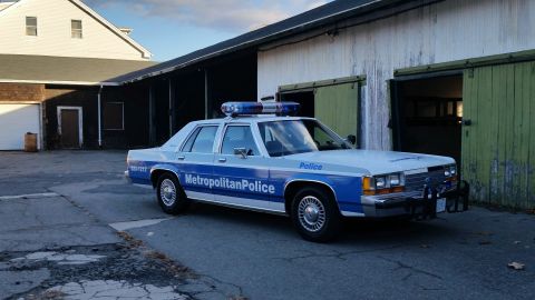 1991 Ford LTD Crown Victoria - A 1991 Ford Crown Victoria police car is parked in front of a barn with its emergency lights on.