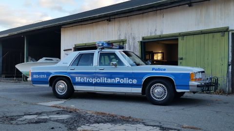 1991 Ford LTD Crown Victoria - Side view of a 1991 Ford Crown Victoria police car parked outside a building.