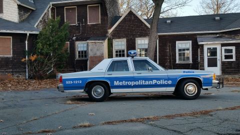 1991 Ford LTD Crown Victoria - Side view of a police car with 'Metropolitan Police' text, parked in front of a derelict building.