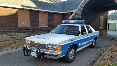 1991 Ford LTD Crown Victoria - A 1991 Ford Crown Victoria police car is parked in front of a weathered building.