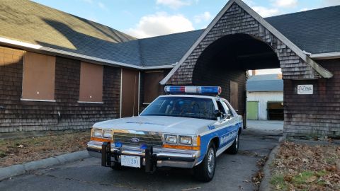1991 Ford LTD Crown Victoria - A 1991 Ford Crown Victoria police car is parked in front of a weathered building with boarded-up windows.