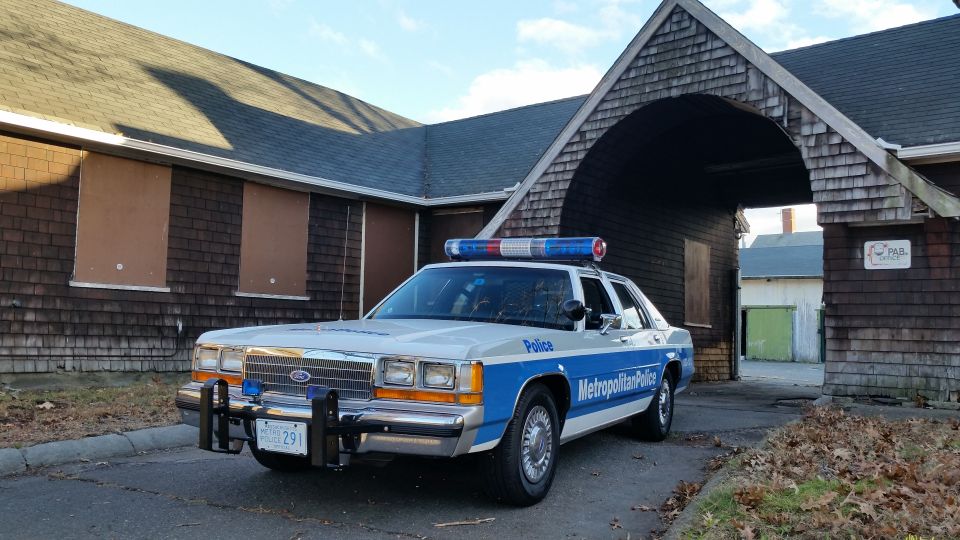 Police car parked in front of a building with boarded up windows. It has 'Metropolitan Police' written on the side