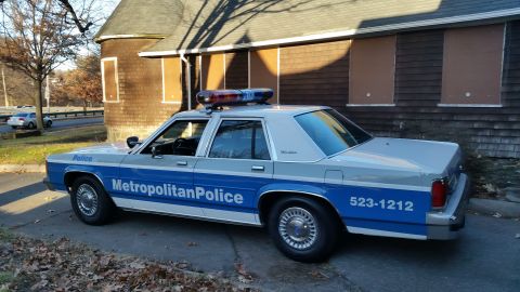 1991 Ford LTD Crown Victoria - A 1991 Ford Crown Victoria police car is parked outside a building with boarded-up windows.