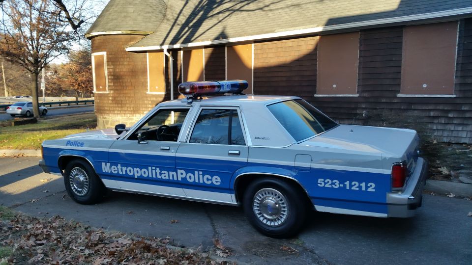 Police car, light bar on roof, 'Metropolitan Police' text on side, parked near a building