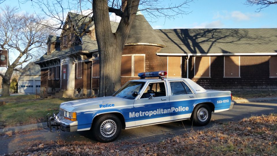 Police car parked in front of a boarded-up house. It's a 1991 Ford Crown Victoria