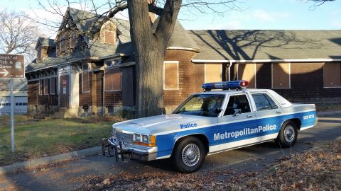 1991 Ford LTD Crown Victoria - A police car is parked in front of an abandoned house.