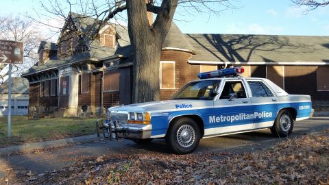 1991 Ford LTD Crown Victoria - A 1991 Ford Crown Victoria police car is parked in front of an abandoned house.