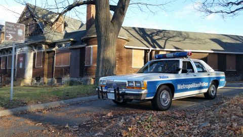 1991 Ford LTD Crown Victoria - Metropolitan Police car parked in front of an abandoned building with boarded windows.
