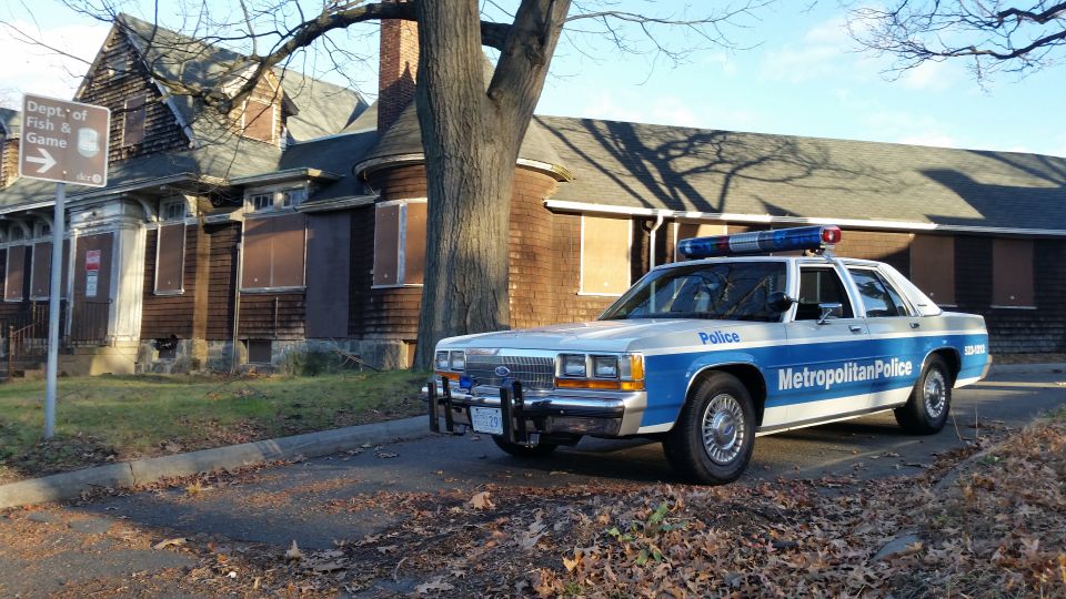 1991 Ford Crown Victoria police car, Metropolitan Police markings, parked on street. Building behind is boarded up