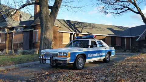 1991 Ford LTD Crown Victoria - A 1991 Ford Crown Victoria police car is parked on a street in front of an old, boarded-up house.