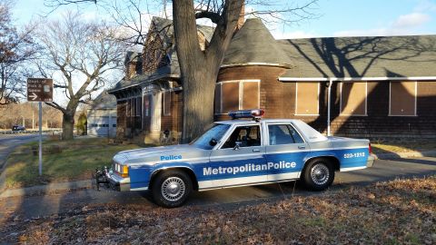1991 Ford LTD Crown Victoria - A 1991 Ford Crown Victoria police car is parked on the side of the road in front of an old building.