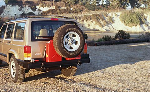1990 Ford Bronco - Gold Jeep Cherokee XJ equipped with a rear-mounted jerrycan and spare tire, parked outdoors.