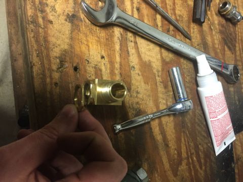 1982 Ford Bronco - A brass fitting is examined with various tools, including a ratchet and wrench, on a workbench.