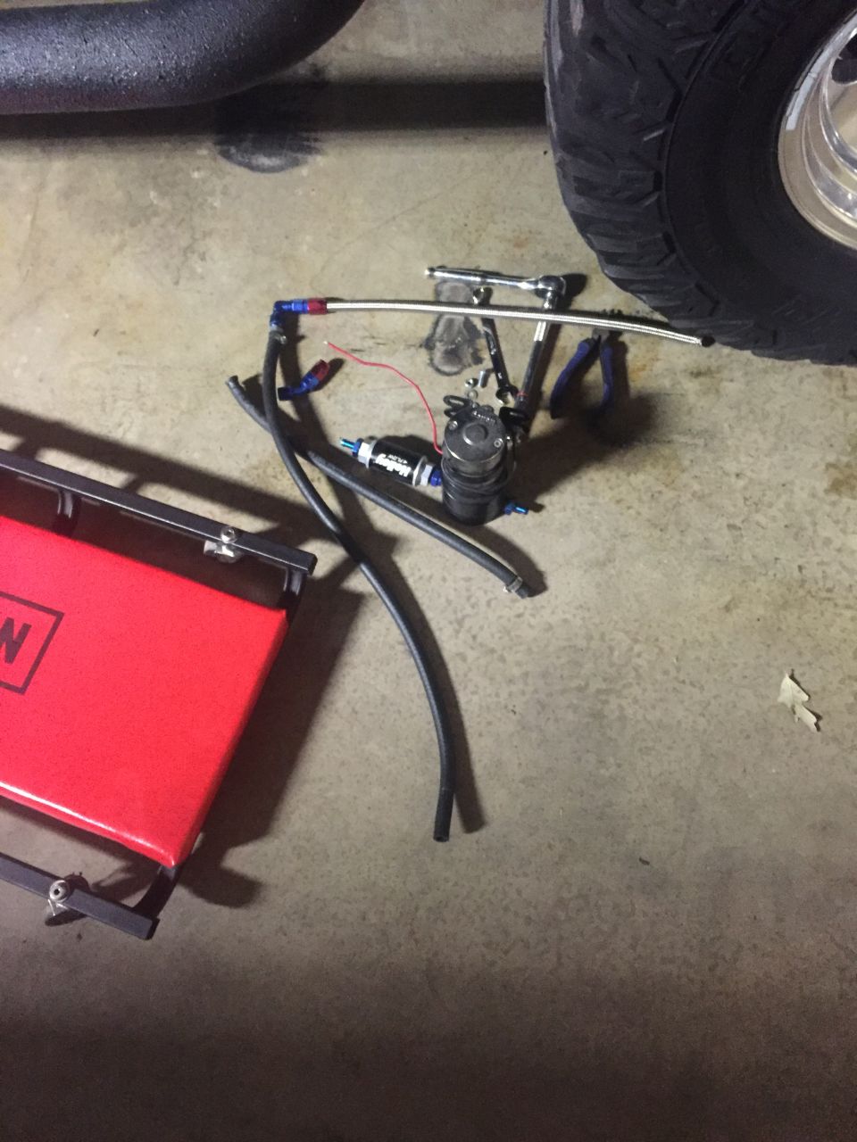 fuel pump, lines, and tools on garage floor next to a tire