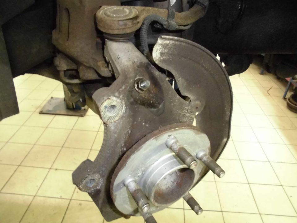 Wheel hub assembly with brake dust shield and suspension linkage, showing rust and wear