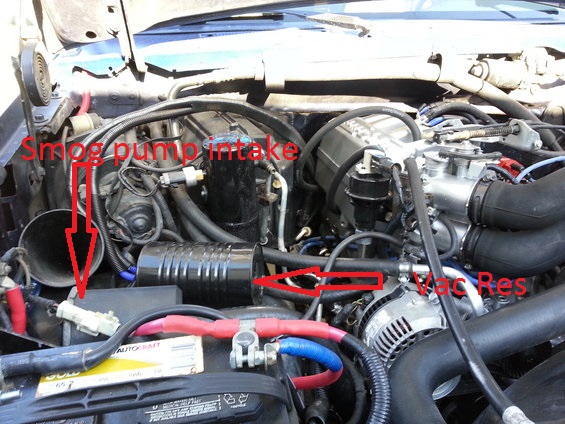 Engine bay showing smog pump intake and vacuum reservoir. Battery terminals are red and blue