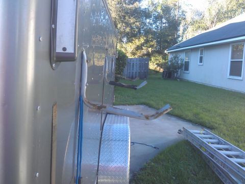 1994 Ford Bronco - A single, rusty ladder rack part is attached to the side of a utility trailer, with a residential house and yard in the background.
