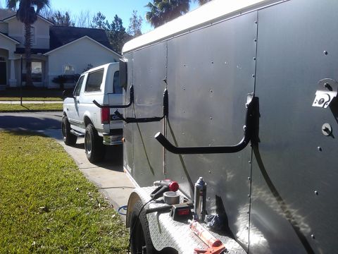 1994 Ford Bronco - A white SUV is parked next to a silver cargo trailer, with tools visible on the trailer's fender.