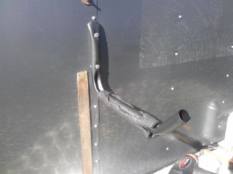 1994 Ford Bronco - A black metal ladder rack component is bolted to a dark, textured wall, with a wooden block for support.