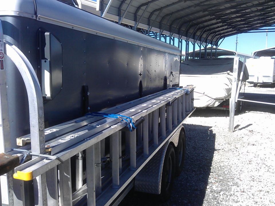Trailer with a ladder rack carrying aluminum ladders, parked under a metal awning