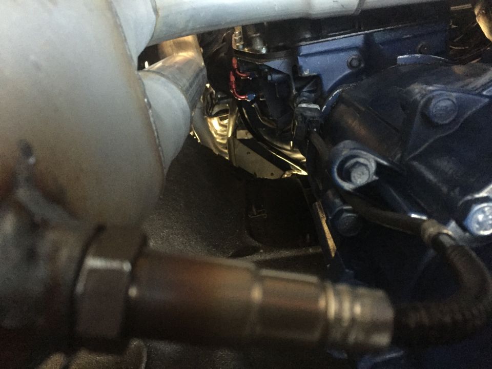Engine bay with exhaust pipe and oxygen sensor in foreground, black engine block and wiring in background